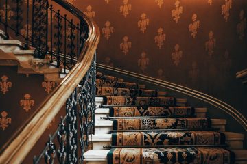 A beautifully detailed vintage staircase with ornate iron handrails and rich patterned carpet.